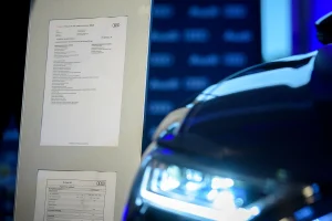 Bemutató rendezvény fotózása a háttérben az Audi leírásával, az előtérben életlenül az autó világító lámpájával.