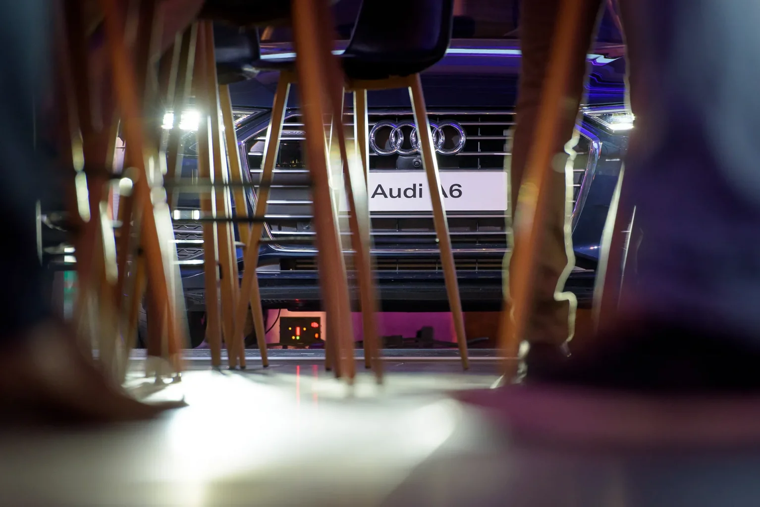 Bemutató rendezvény fotózása az Audi A6-al a háttérben békaperspektívából fotózva, az előtérben rendezvény székeinek lábaival.