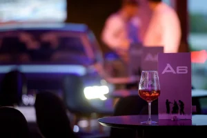 Rosé bor pohárban, a háttérben elmosódva világító lámpákkal az Audi.