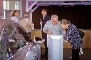 Egy férfi és egy nő közelebbről nézik az autó paramétereit, a rendezvényen kihelyezett ismertetőn.
