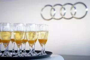 Pezsgő, poharakba kitöltve a rendezvényen, a háttérben elmosódva az Audi logoja.