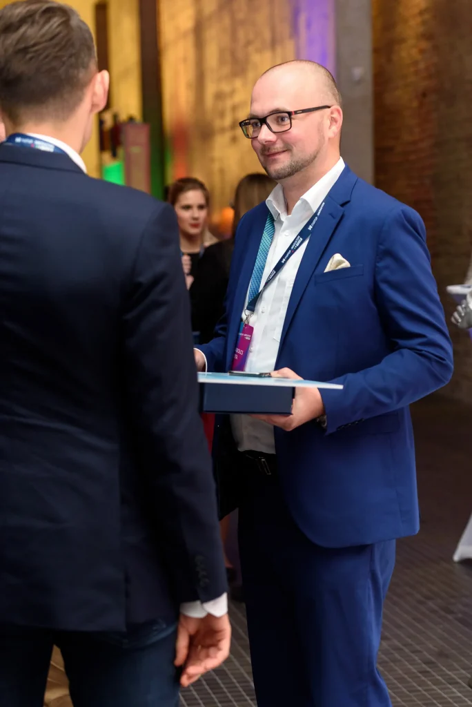 Konferencia fotózás Budapest egy szemüveges férfi kék öltönyben, kigombolt zakóban beszélget egy másikkal.